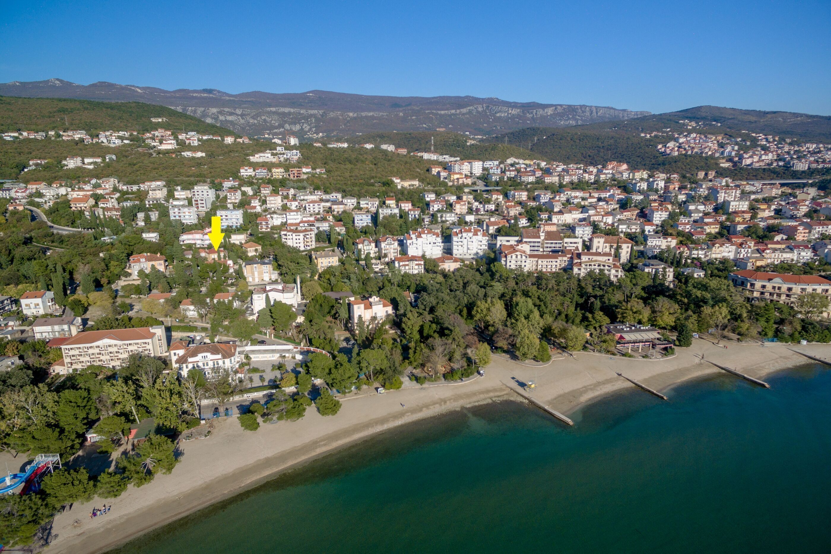An aerial view of a coastal town with a beach, residential buildings, and a prominent yellow building.