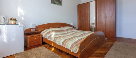 A bedroom with a wooden bed, a nightstand, a wardrobe, and a small table with a lamp.