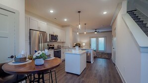 A modern kitchen with white cabinetry, a central island, and a dining area with a wooden table and chairs. - *2bd/2.5bth | Near Downtown| Soccer Stadium* #D (Nashville)