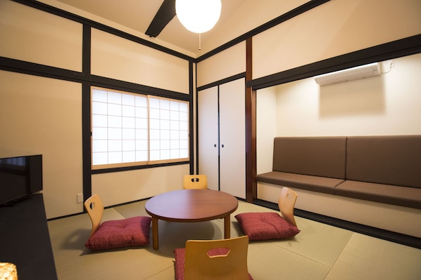 A traditional Japanese room with tatami flooring, a tatami mat table, a low brown sofa, and a sliding door with a grid pattern.