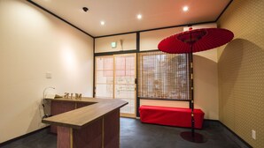 A reception area with a wooden desk, a red bench, a traditional red umbrella, and sliding doors with a decorative screen. - Benifuji-ann (Kyoto)