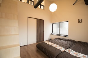 A bedroom with a bed, wooden flooring, a window, and a door.