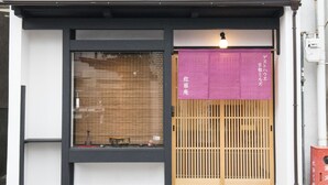 A traditional Japanese building with a wooden sliding door, a display window with various items, and a purple hanging sign with white text. - Benifuji-ann (Kyoto)