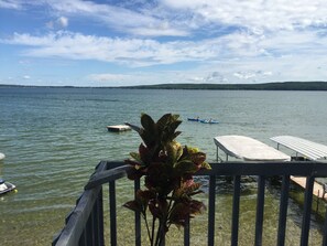 A lake view from a balcony with a dock, a small boat, and a covered seating area. - Beautiful Hubbard Lake Waterfront Cottage 1 (Hubbard Lake)