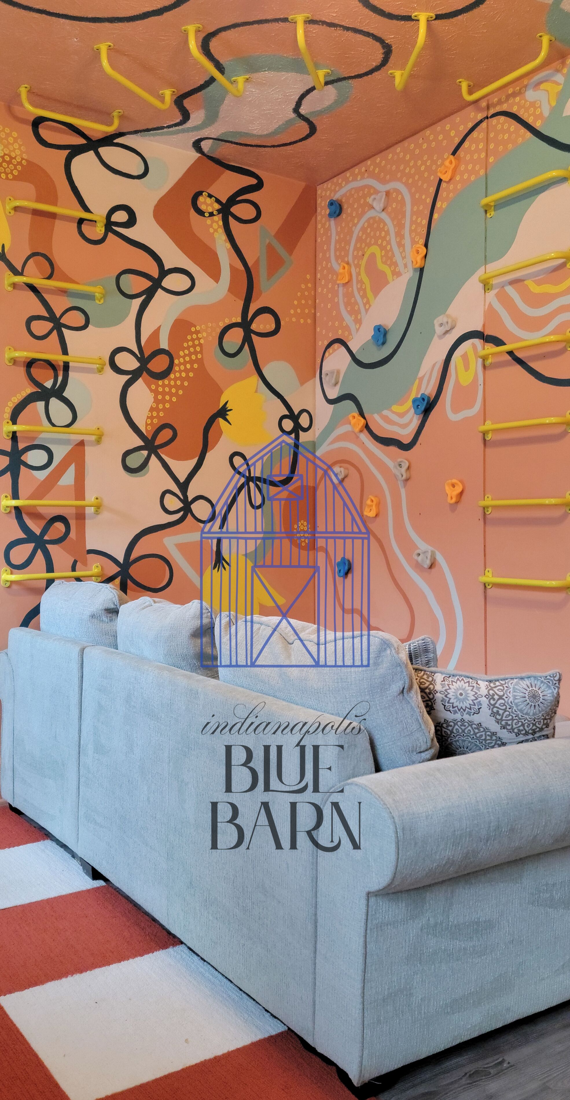 A room with a light blue sofa, a red and white striped rug, and a wall with abstract art and climbing holds.