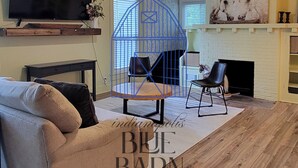 A living room with a sofa, a TV, a ceiling fan, a fireplace, and a blue barn-themed chair.