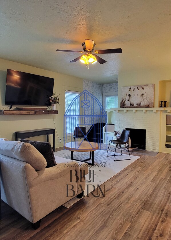 A living room with a sofa, a TV, a ceiling fan, a fireplace, and a blue barn-themed chair.