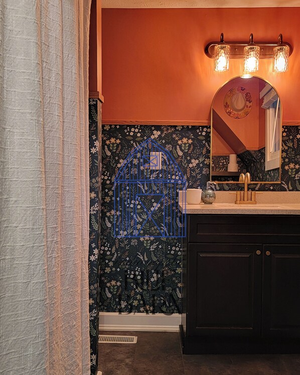 A bathroom with a dark floral wallpaper, a blue birdcage decoration, a white sink with gold fixtures, and a mirror with a decorative frame.