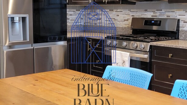 A modern kitchen with dark wood cabinets, stainless steel appliances, and a wooden dining table with blue chairs.
