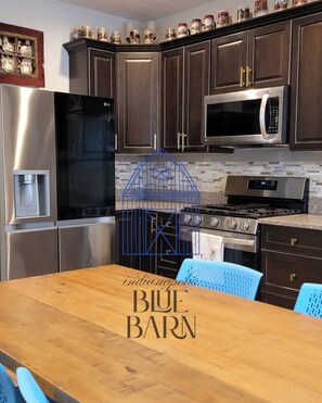 Una cocina moderna con armarios de madera oscura, electrodomésticos de acero inoxidable y una mesa de comedor de madera con sillas azules.