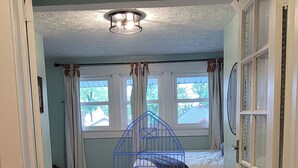 A bedroom with a bed, a window with curtains, a white rug, and a door.