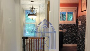 A hallway with a wooden floor, a chandelier, and a view into a room with a window and a door.