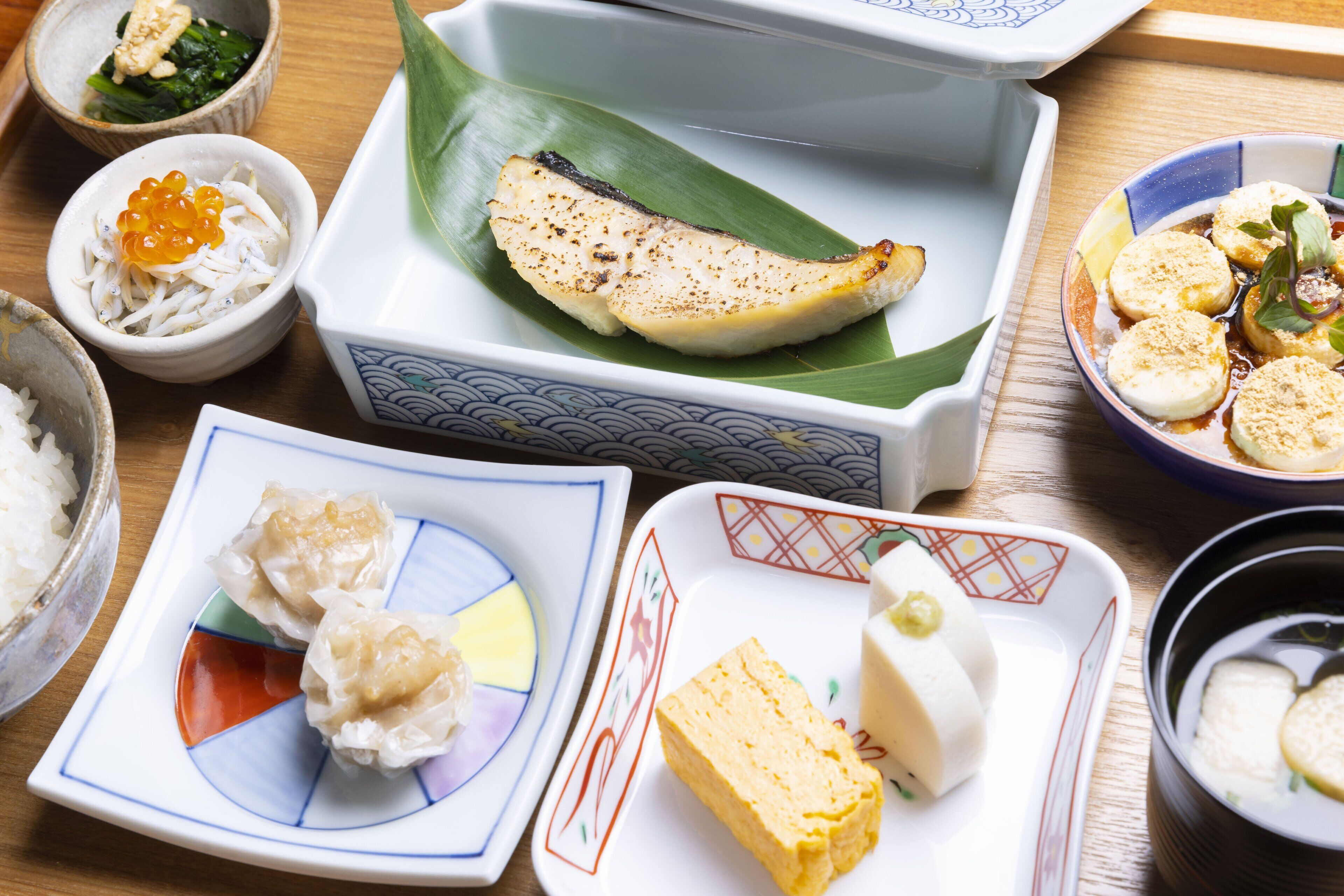 Verschiedene japanische Gerichte, darunter Sushi, Sashimi und eingelegtes Gemüse, auf einer Holztisch.
