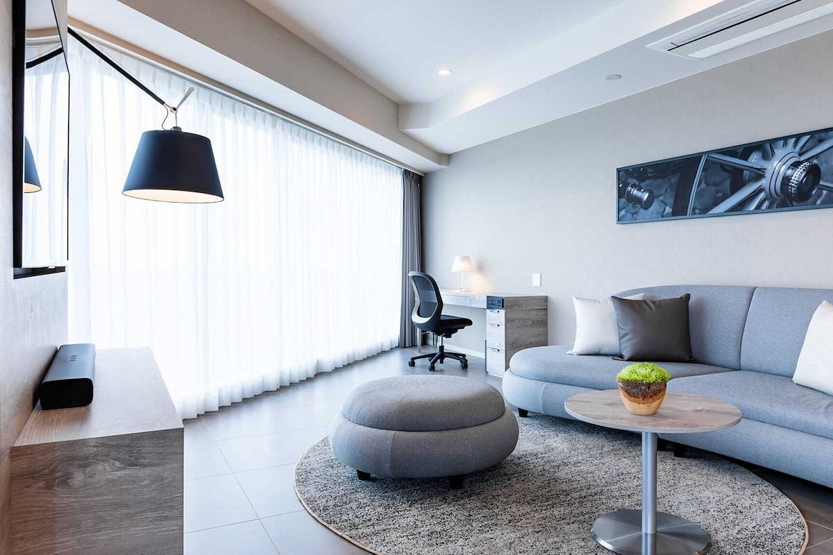 A modern living room with a grey sofa, a round coffee table, and a large window with sheer curtains.