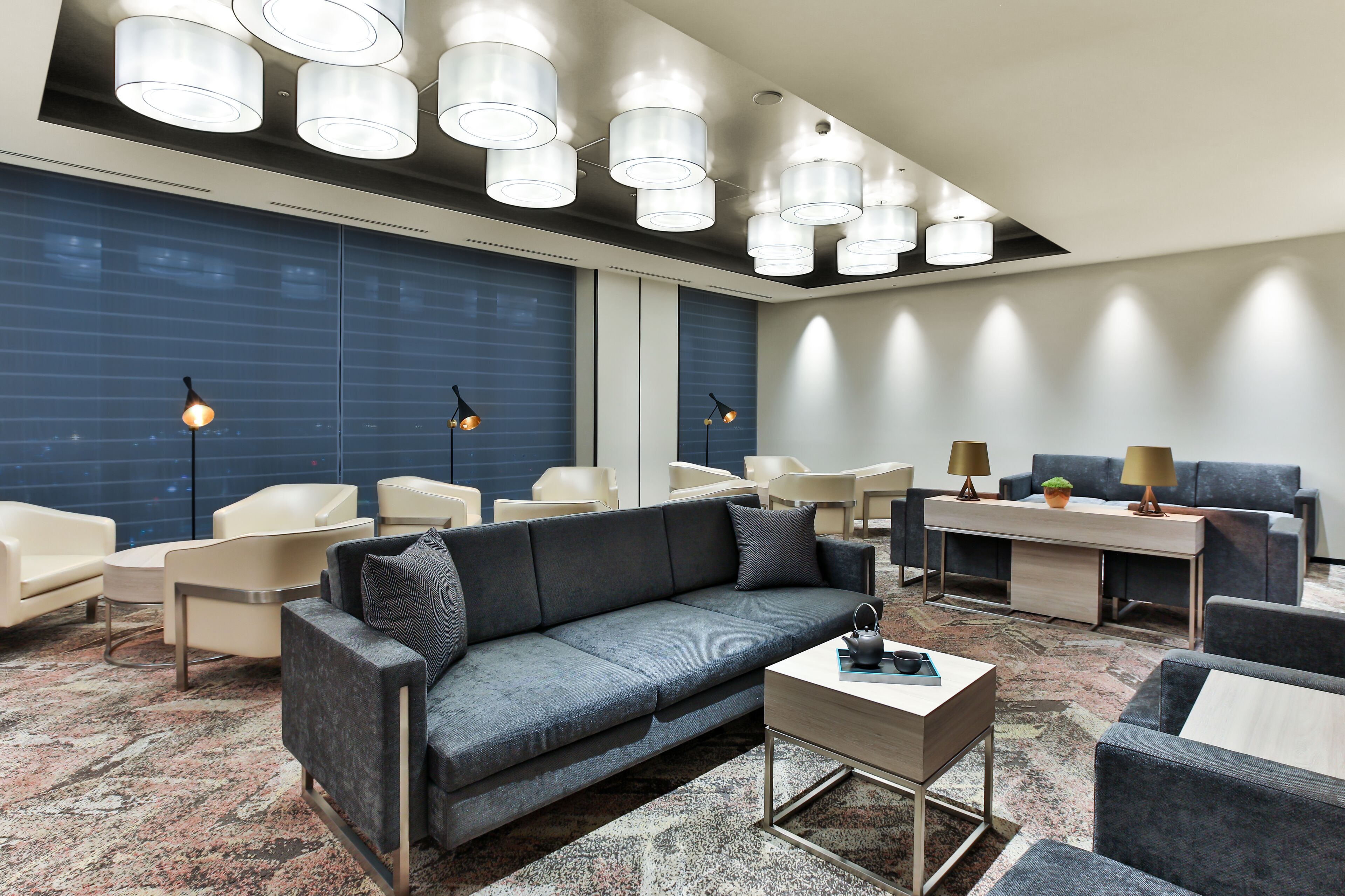 En moderne lobby med en grå sofa, hvide lænestole, et sofabord og et skrivebord med lamper.