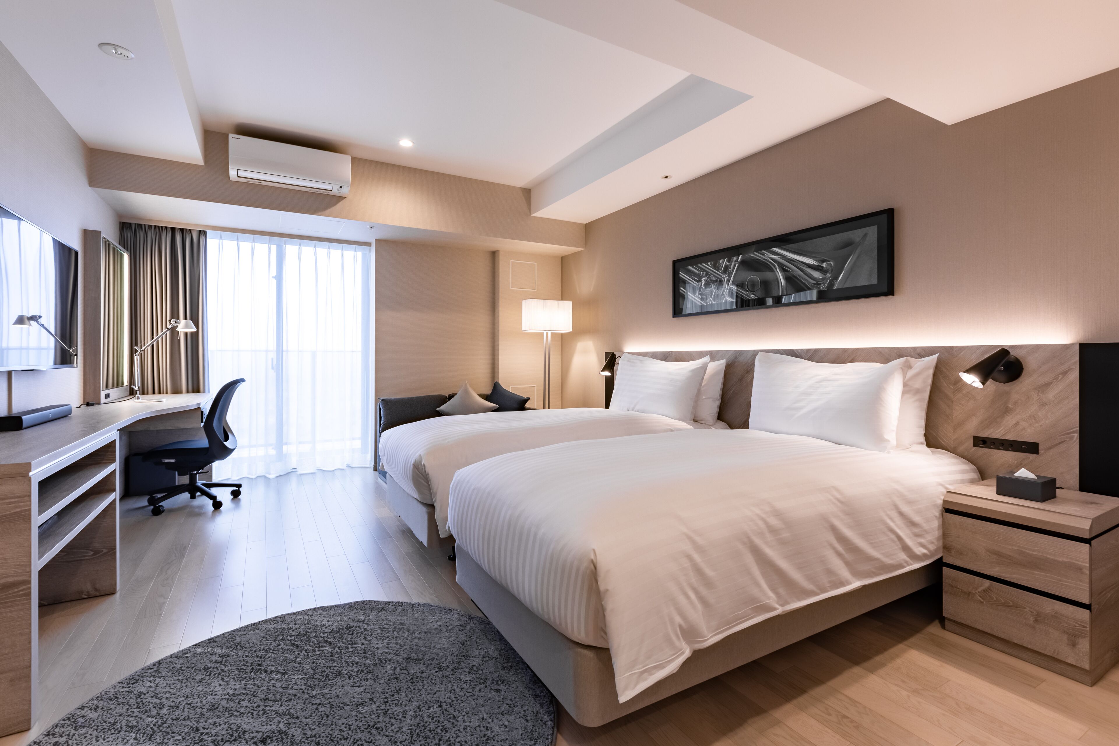 A modern hotel room with a large bed, a desk, a chair, and a flat-screen TV.