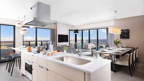 A modern kitchen with a large island, a dining area with a view, and a large window overlooking a cityscape.