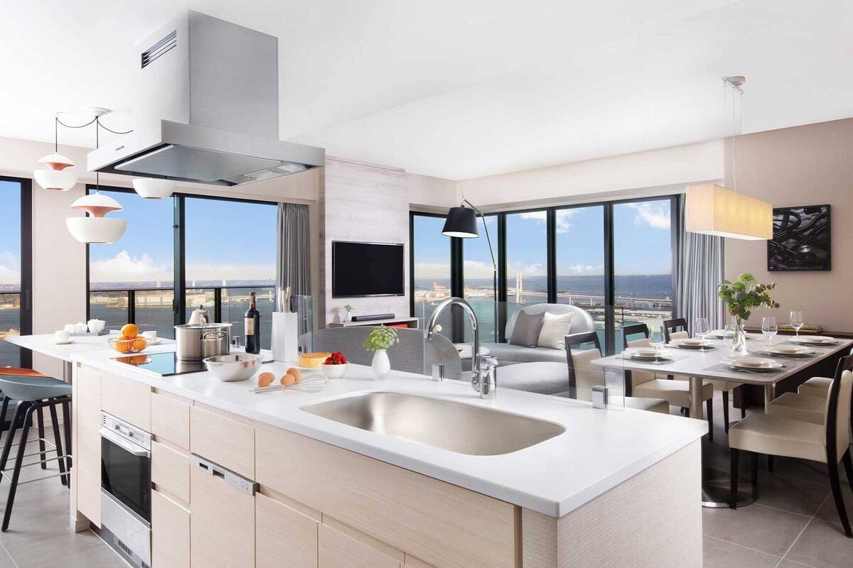 A modern kitchen with a large island, a dining area with a view, and a large window overlooking a cityscape.