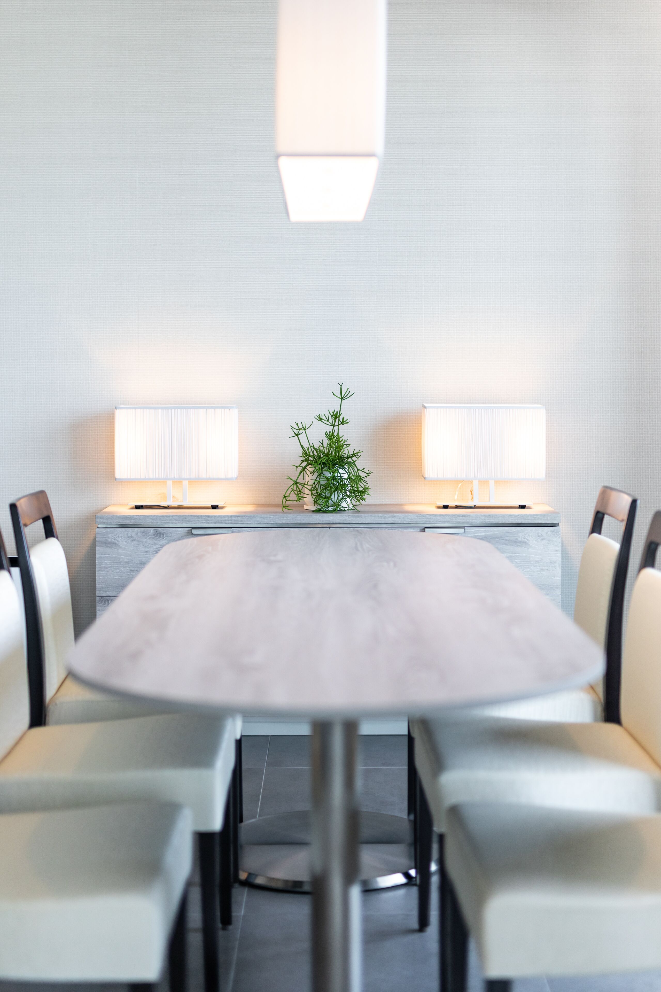 A modern conference room with a round table, white chairs, two wall-mounted lamps, and a small potted plant.