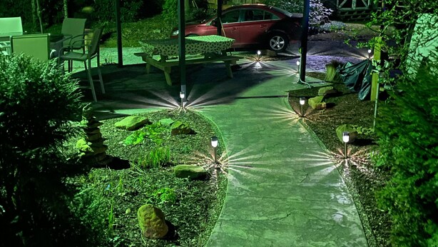 A nighttime outdoor area with a paved walkway, a covered seating area, and a red car parked nearby. - Entire Cottage with Additional Creek Cabin - Fallingwater Ohiopyle Seven Springs (Normalville)