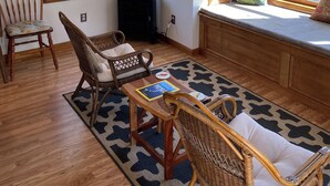 A cozy room with a wooden ceiling, large windows with a view of trees, a comfortable seating area with wicker chairs and a table, and a built-in bench with cushions. - Entire Cottage with Additional Creek Cabin - Fallingwater Ohiopyle Seven Springs (Normalville)