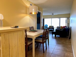 Uma área de refeições com mesa branca, cadeiras de madeira e luminária pendente.