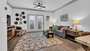 A living room with a sofa, coffee table, and a television. There are vinyl records on the wall and a ceiling fan.