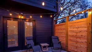 A patio with two chairs and a small table, a wooden fence, and string lights.