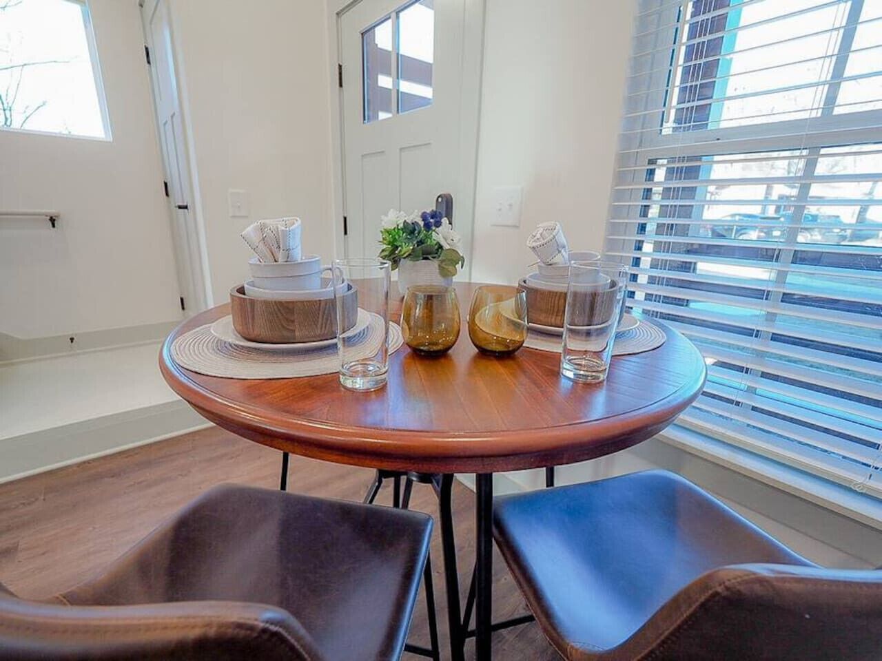 A round wooden table with a vase of flowers, two bowls, and several glasses.