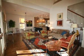 Ein geräumiges Wohnzimmer mit einer Couch, Sesseln, einem Couchtisch und einem Teppich. Eine Treppe führt zu einer oberen Ebene.