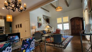 Un vaste salon agrémenté d’un lustre, un coin repas avec des chaises colorées, un plancher en bois et une grande armoire en bois.