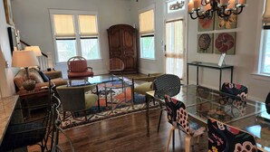 Un salon spacieux avec une table basse en verre, plusieurs fauteuils, un meuble en bois et un lustre.
