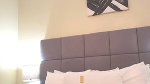 A neatly made bed with white linens, a bottle of alcohol, and folded towels on a headboard.