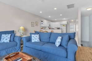A living room with a blue sofa set, a wooden coffee table, and a kitchen in the background.