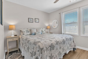 A bedroom with a bed, two bedside tables, a nightstand, a wall clock, and a window with blinds.