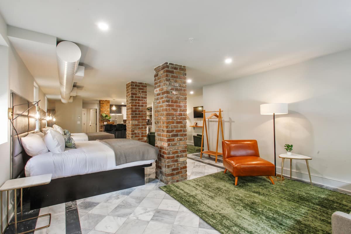 A modern bedroom with a bed, a green rug, a brick pillar, and a leather chair.