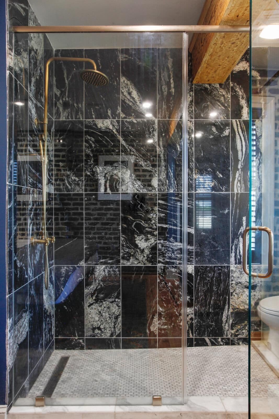 A modern shower enclosure with a glass door, black and white marble tiles, and a visible showerhead.