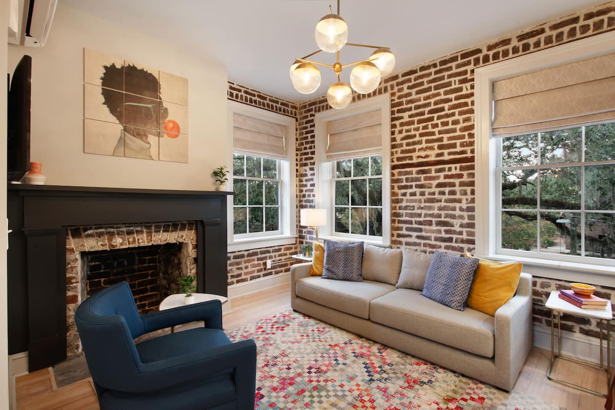 A living room with a brick wall, a sofa, a blue chair, a fireplace, and a large window.