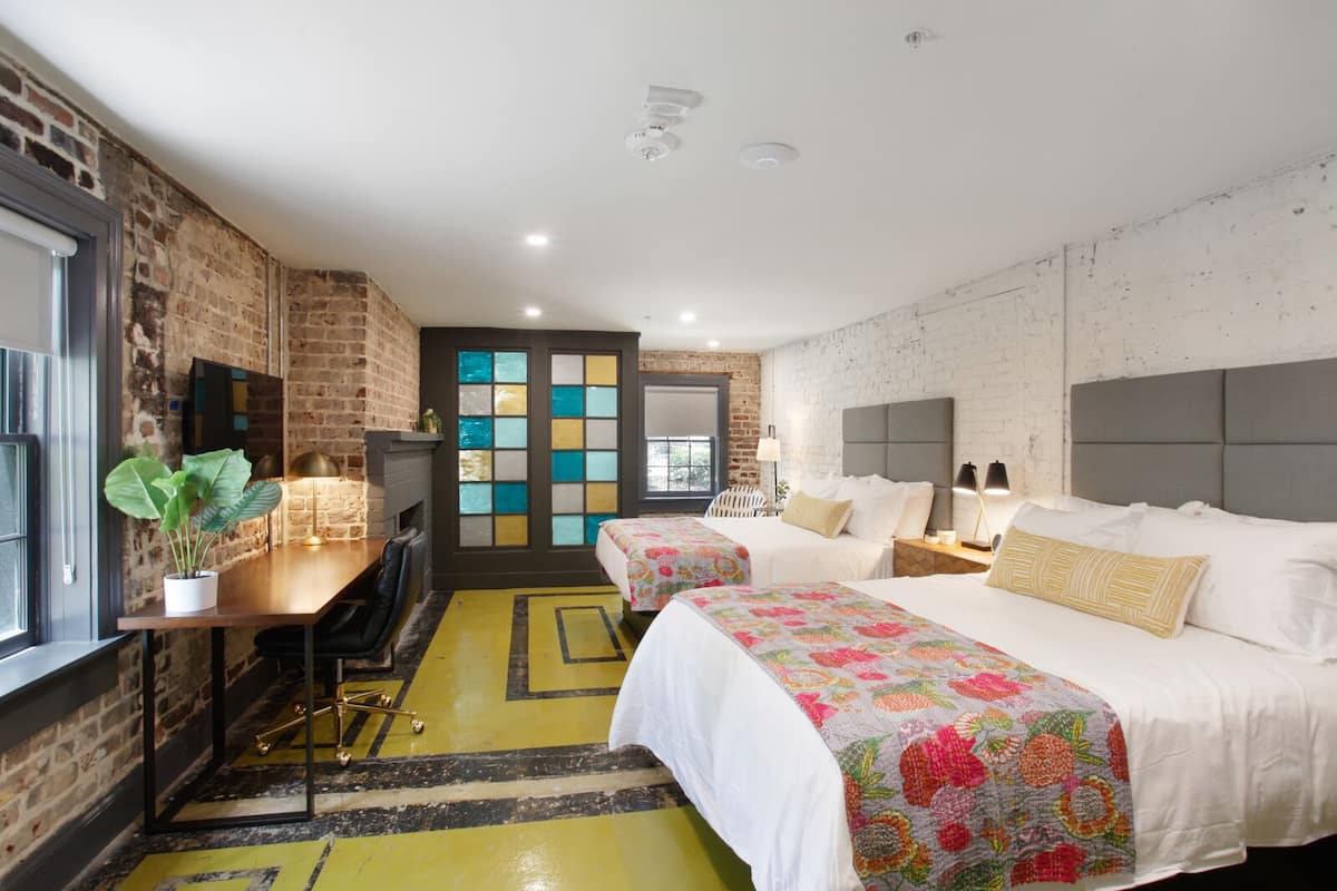 A hotel room with two beds, a desk, and a brick wall.