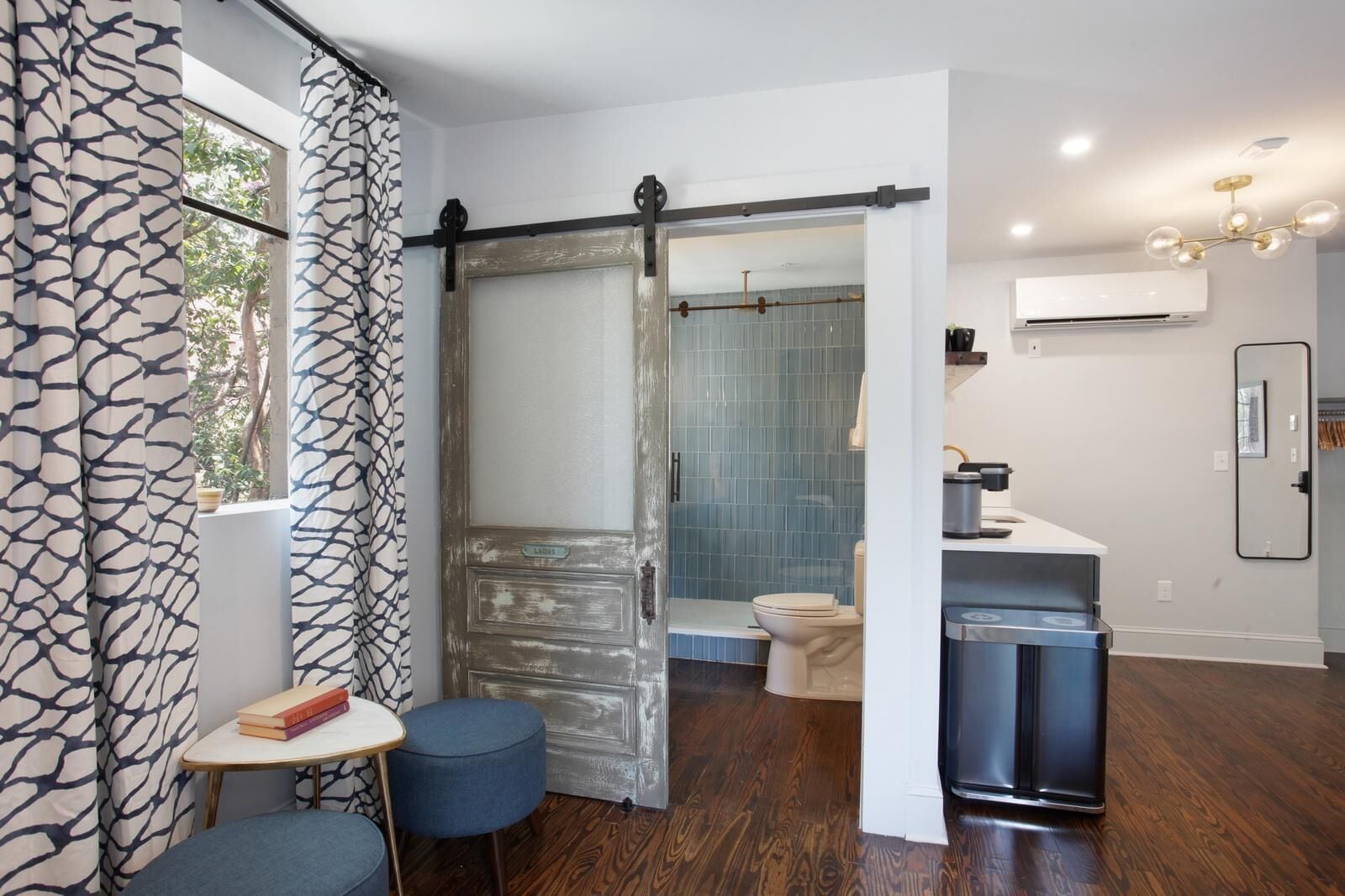 A modern bathroom with a sliding door, a toilet, a sink, and a small table with books.