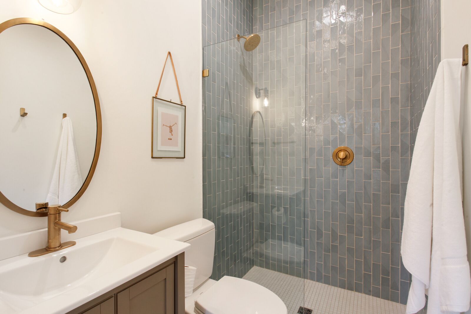 A bathroom with a white sink, a gold-framed mirror, a toilet, and a glass-enclosed shower with a gold showerhead.