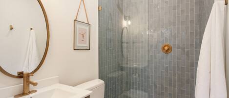 A bathroom with a white sink, a gold-framed mirror, a toilet, and a glass-enclosed shower with a gold showerhead.