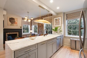 Une cuisine moderne dotée d’un grand îlot central, de luminaires suspendus et d’un mur d’accent en briques.
