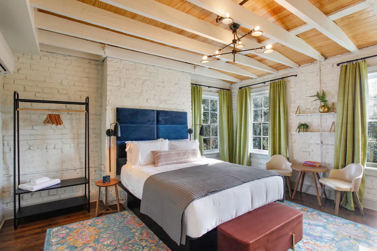 A bedroom with a bed, bedside tables, a hanging rack, a bench, and a window with curtains.