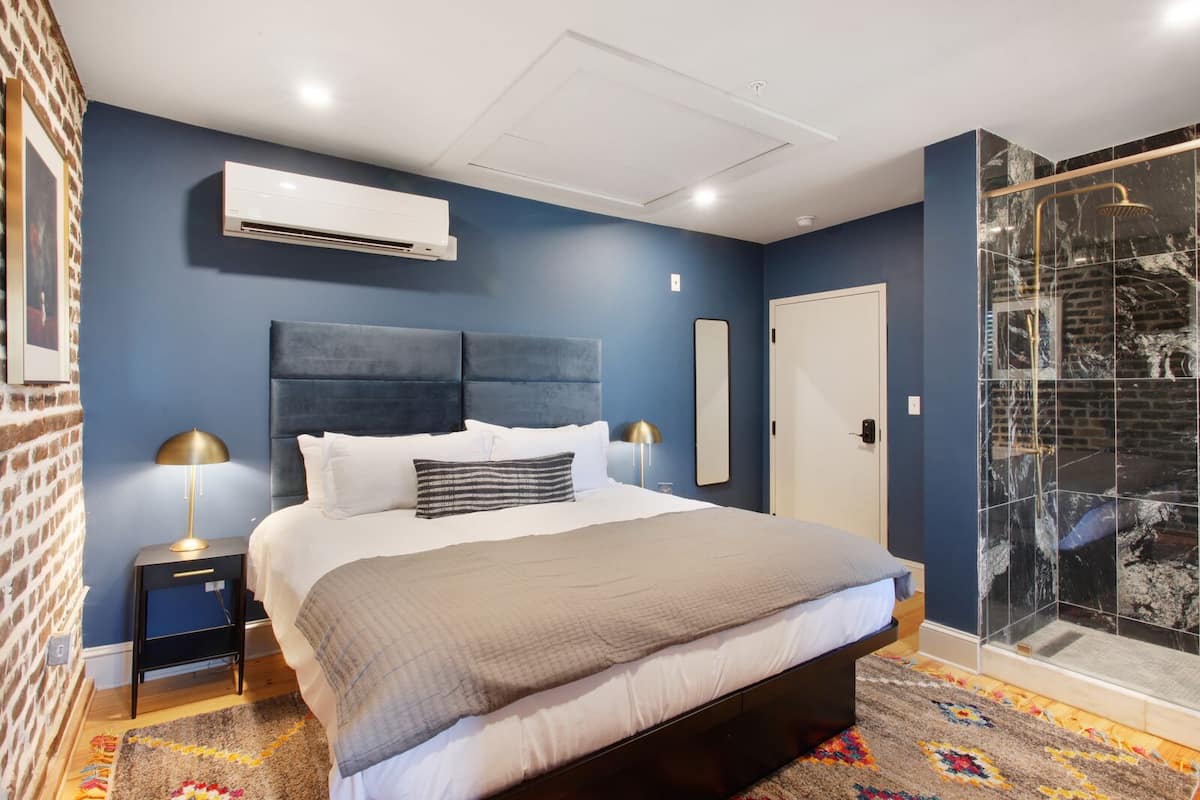 A modern bedroom with a large bed, a glass shower enclosure, and a brick accent wall.