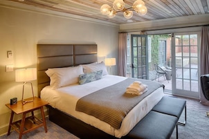 Une chambre d’hôtel avec un grand lit, des lampes de chevet, un banc et une vue sur la terrasse extérieure.