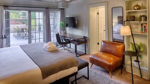 A hotel room with a large bed, a desk, a leather chair, a TV, and a bookshelf. - The Present Hotel (Savannah)