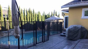 Un pati darrere amb piscina, una zona de terrassa coberta i un recinte tancat per una tanca.