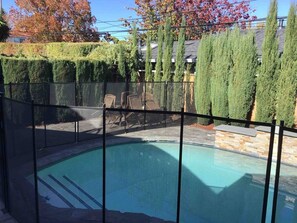 A swimming pool with a surrounding fence, a stone wall, and a hedge.