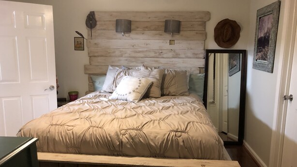 A bedroom with a wooden headboard, a bed with beige bedding, a bedside table, and a mirror.